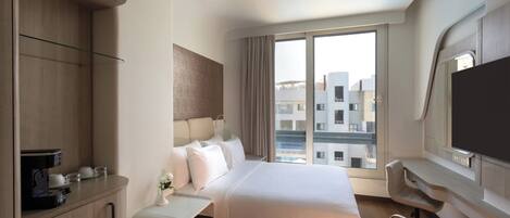 A modern hotel room with a bed, a desk, a chair, a TV, and a window with a city view.