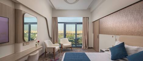 A hotel room with a large bed, a desk, a chair, a TV, and a view of the city.