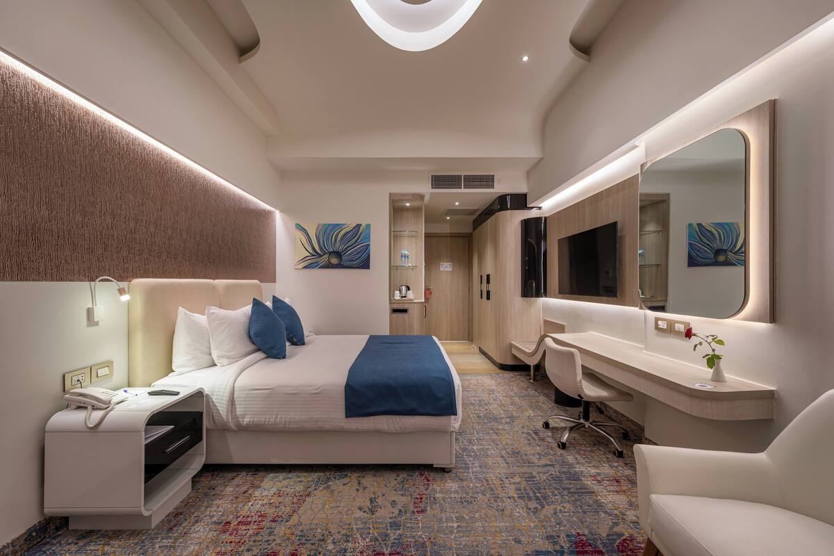 Ein modernes Hotelzimmer mit einem großen Bett, einem Schreibtisch, einem Stuhl, einem Spiegel und Bildern an den Wänden.