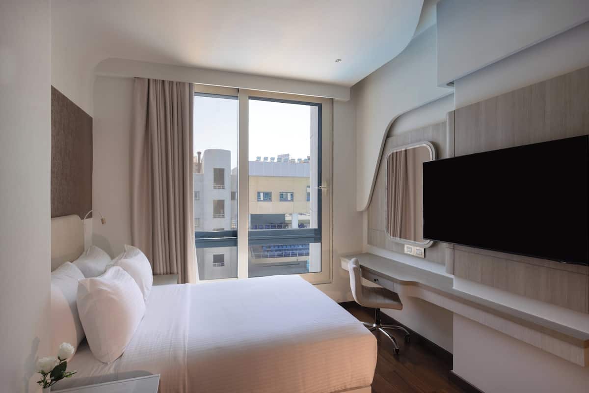 Ein Hotelzimmer mit einem großen Bett, einem Schreibtisch, einem Flachbildfernseher und einer Glastür zum Balkon.