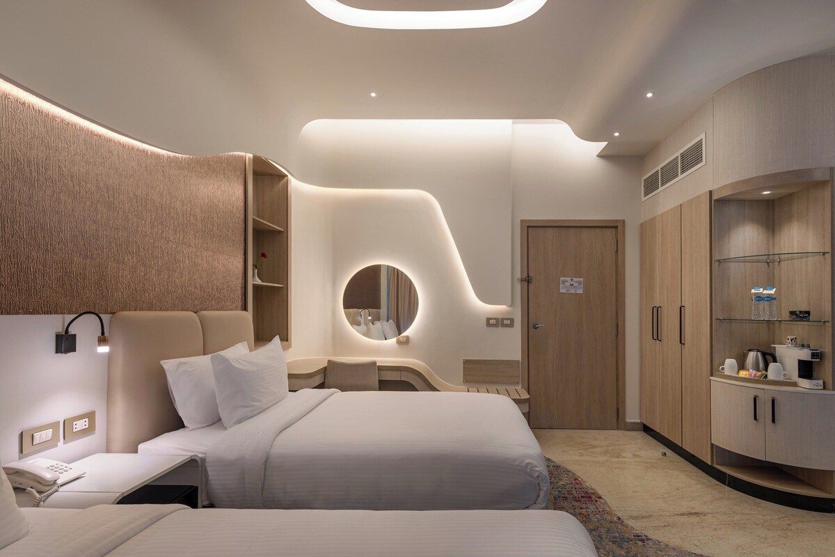 A modern bedroom with a curved headboard, a bedside telephone, a round mirror, and built-in wardrobes.