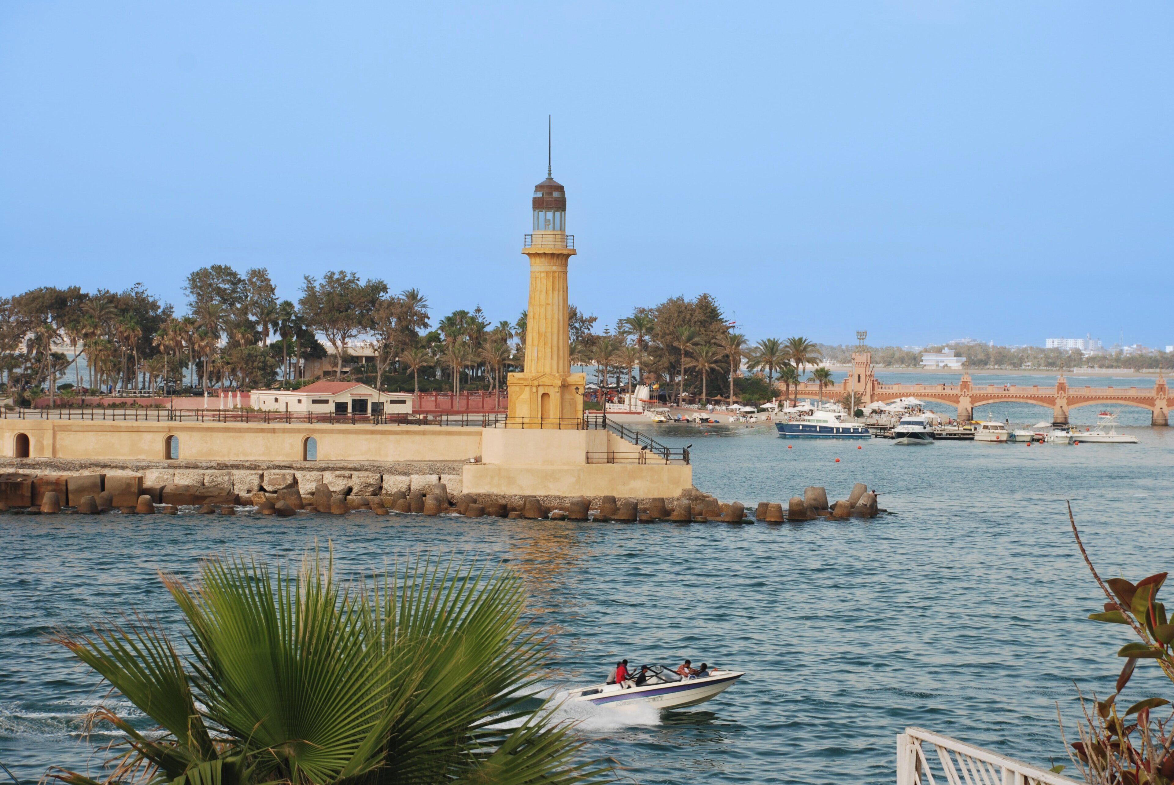 A coastal scene with a prominent yellow lighthouse, a bridge, and boats on the water.