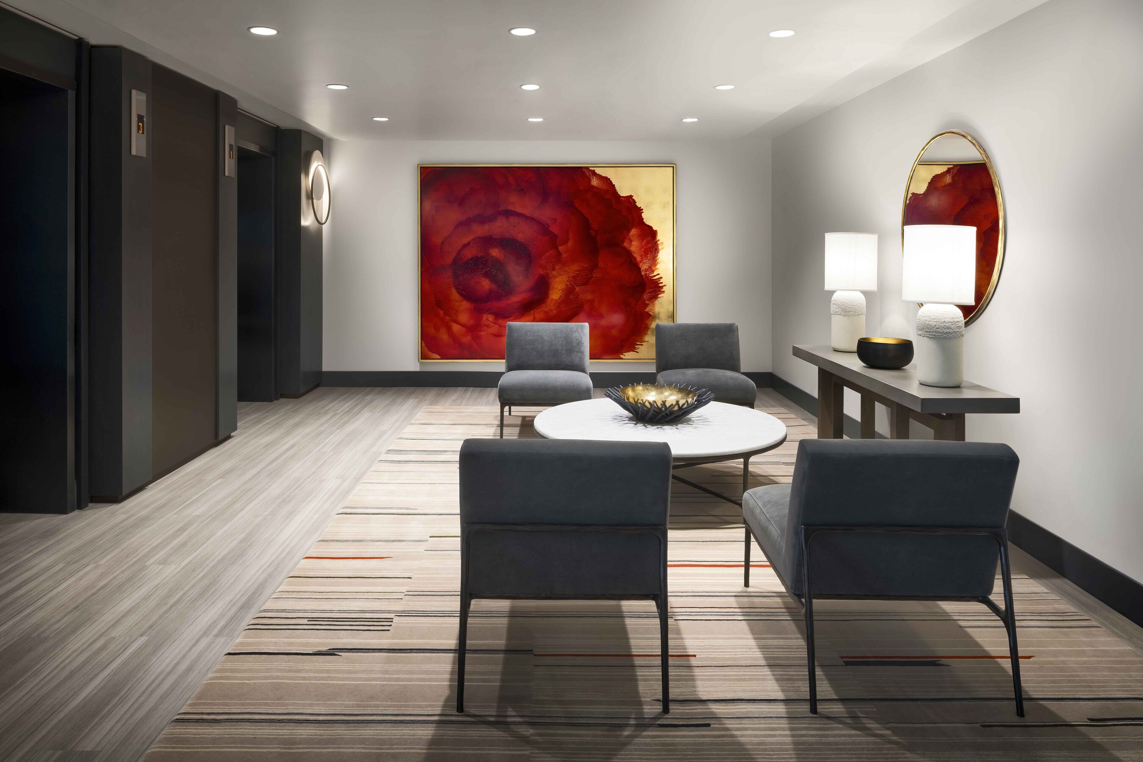 A modern hotel lobby with a large abstract painting, two armchairs, a round table, and a mirror.