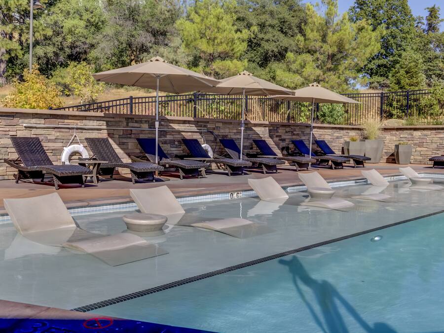 Zona de piscina con sillones de descanso y sombrillas, rodeada de muros de piedra y árboles.