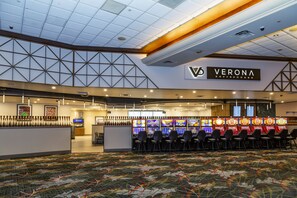 A casino area with multiple slot machines, a reception desk, and a ceiling with geometric patterns.