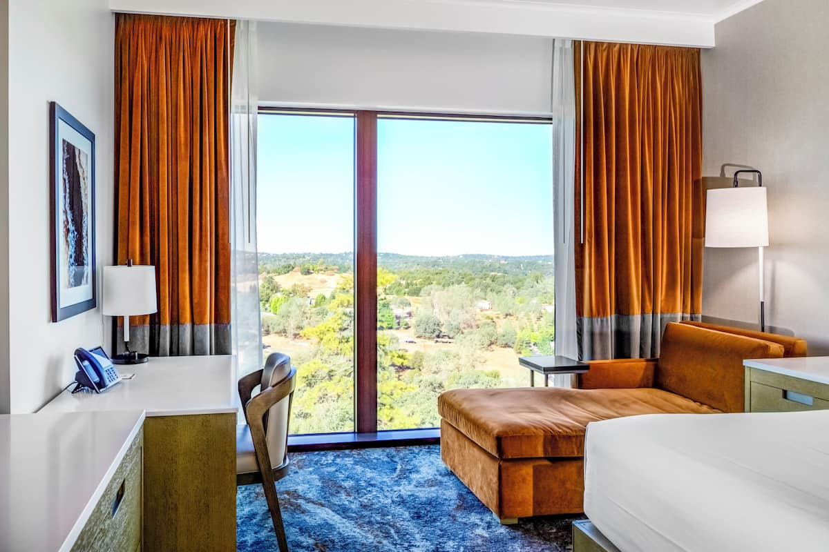Una habitación de hotel con un ventanal grande, un escritorio, una silla, una cama y una mesita.