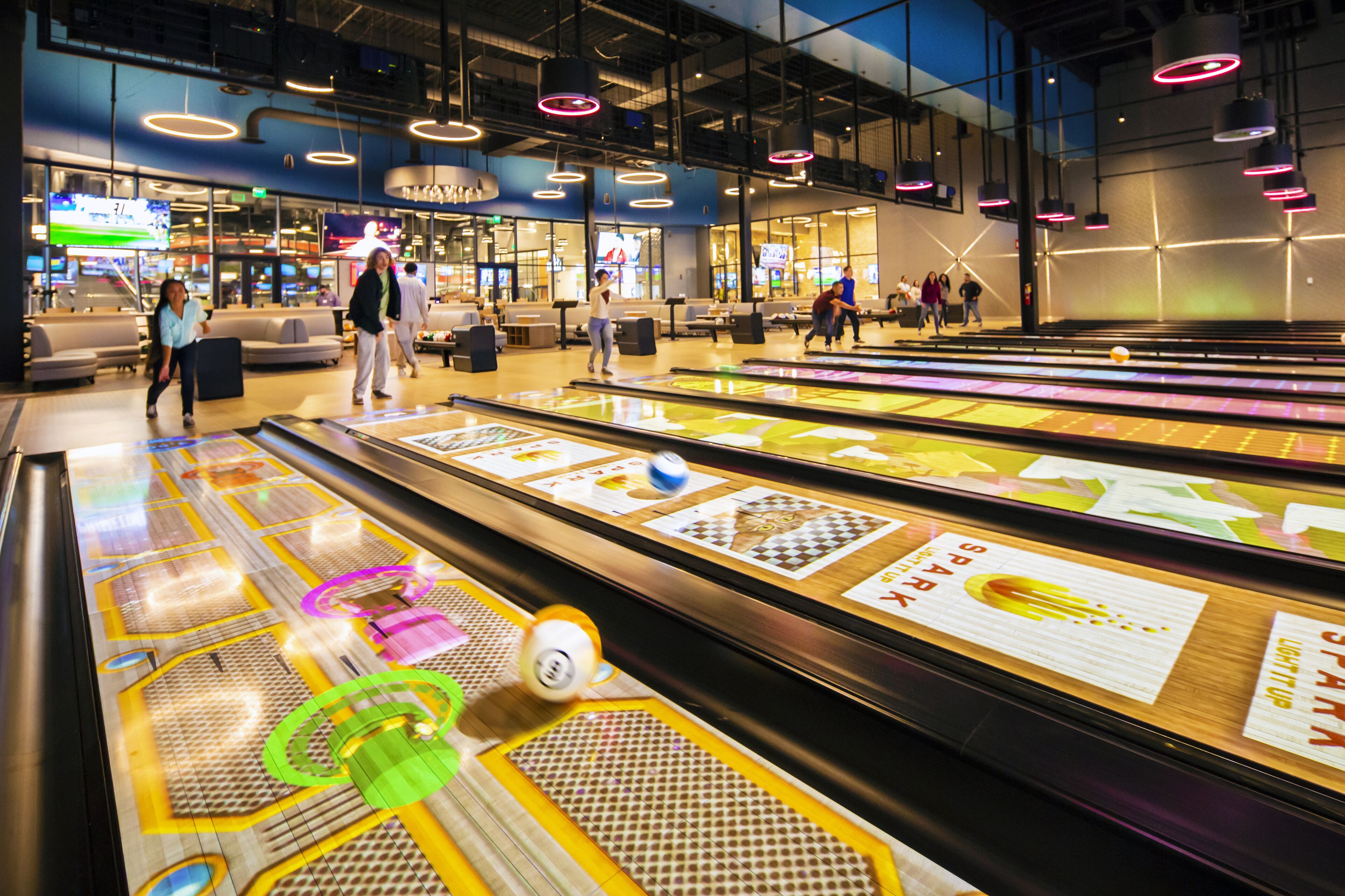 A bowling alley with multiple lanes, a seating area, and overhead lighting.