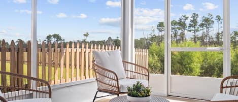 A covered patio with wicker furniture and a view of a wooden fence and greenery.