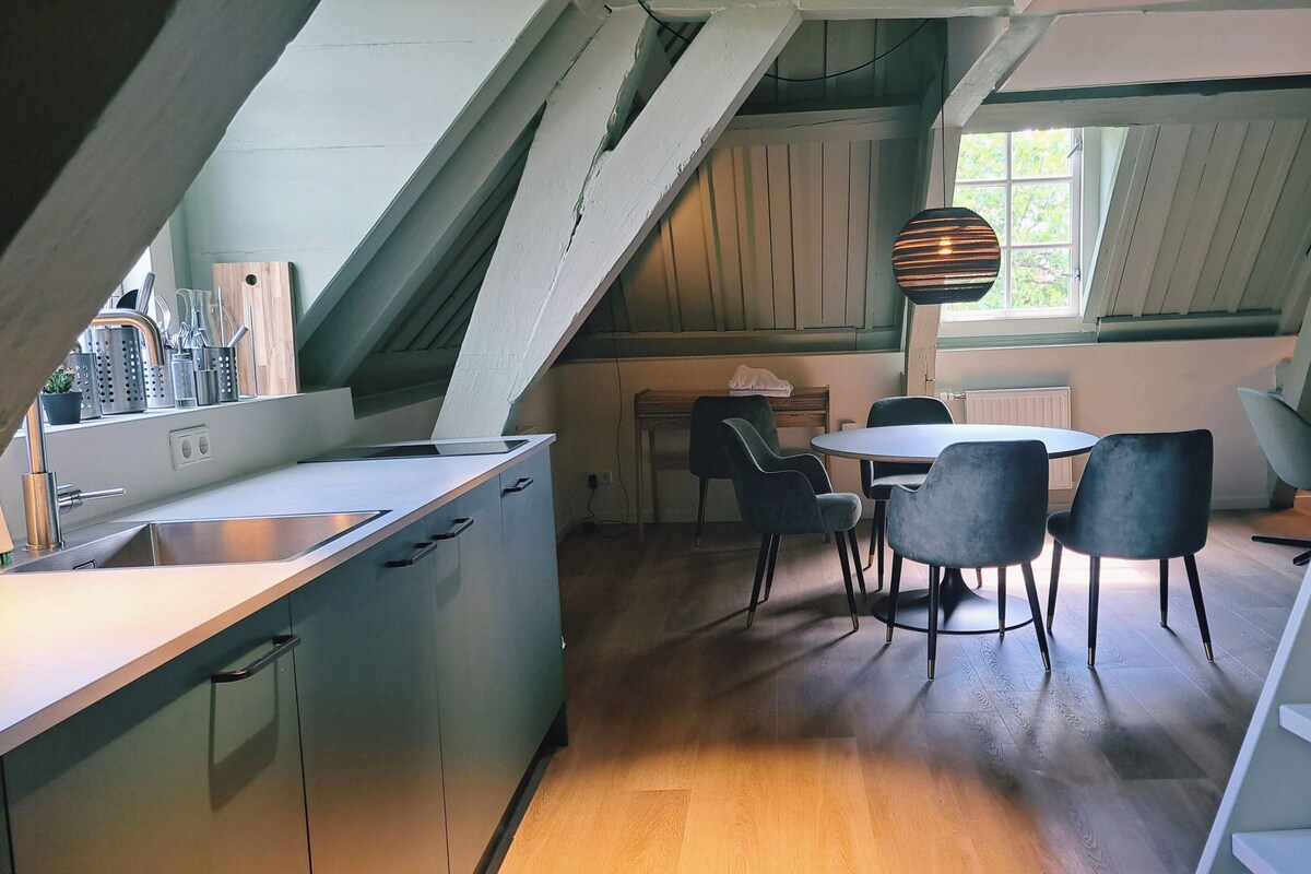 Modernilla designilla varustettu keittiö, ruokailutila pyöreällä pöydällä ja neljällä tuolilla sekä ikkuna, josta tulee luonnonvaloa.