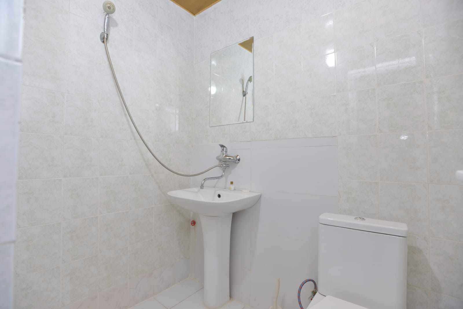 Een badkamer met een wit wastafel, toilet en douche met een handdouche.