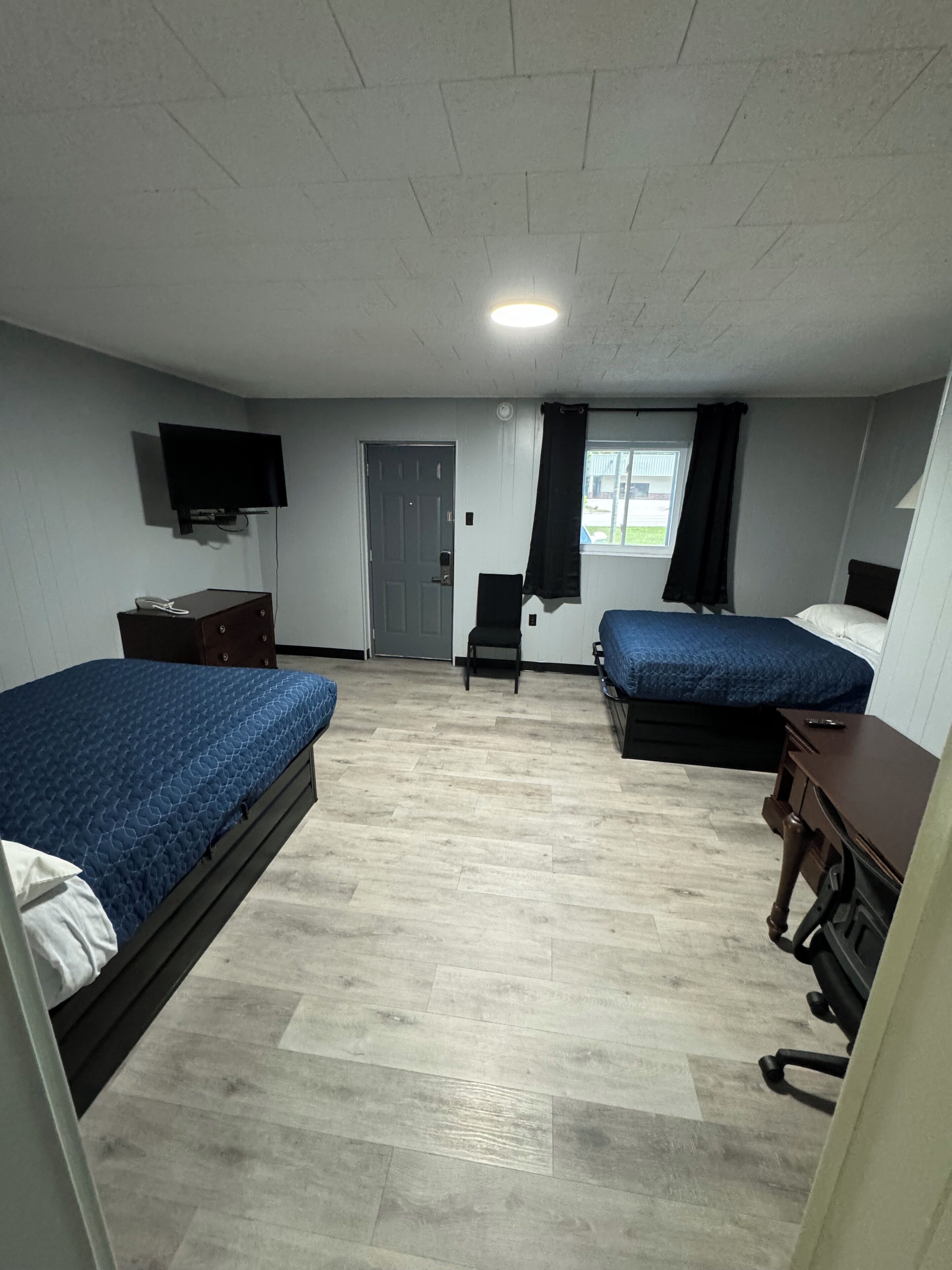 Ein Zimmer mit zwei Betten, einem Schreibtisch, einem Stuhl, einem Fernseher und einer Tür.