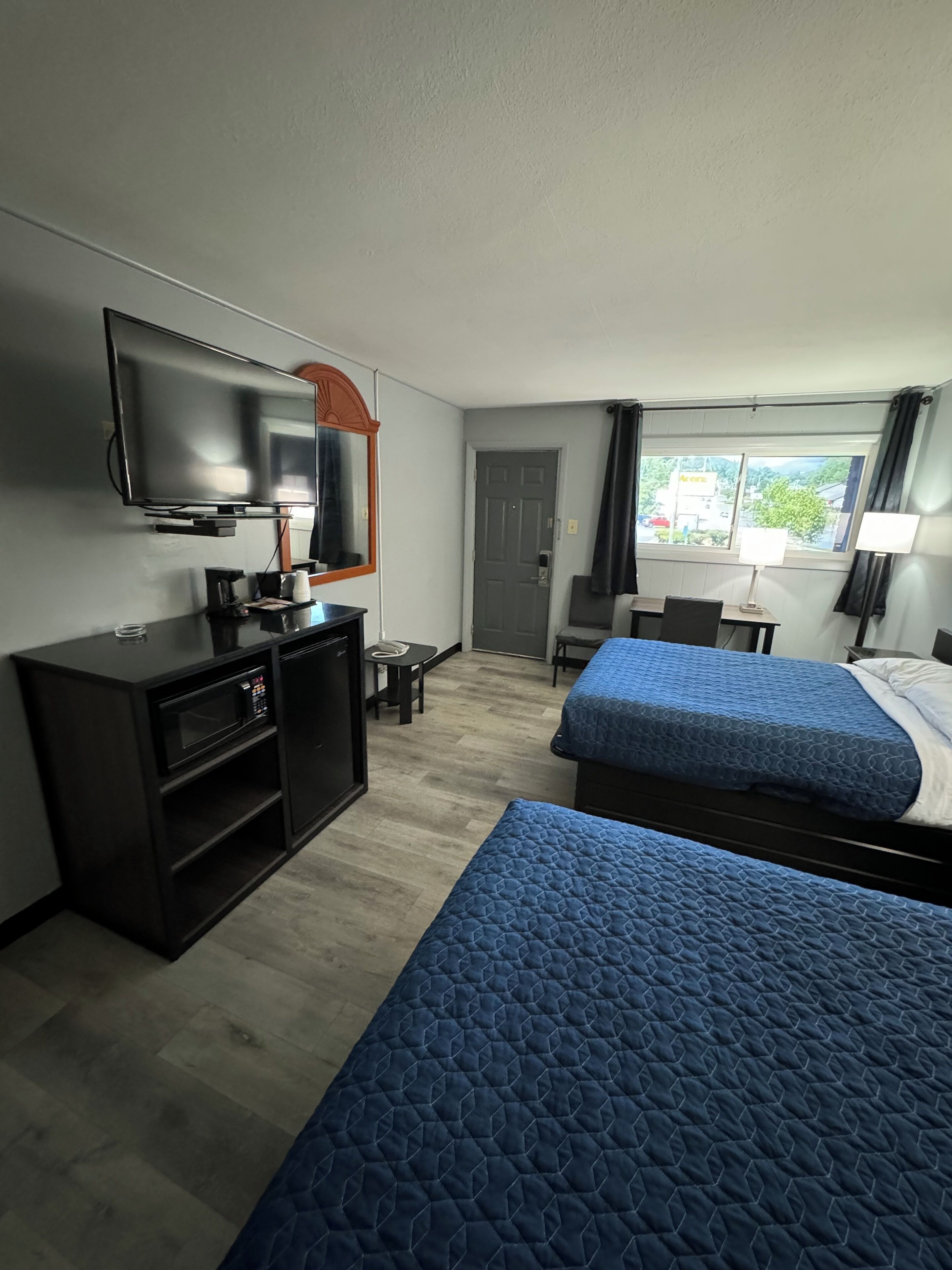 Ein Hotelzimmer mit zwei Betten, einem Fernseher, einem Schreibtisch und einem Fenster mit Blick.