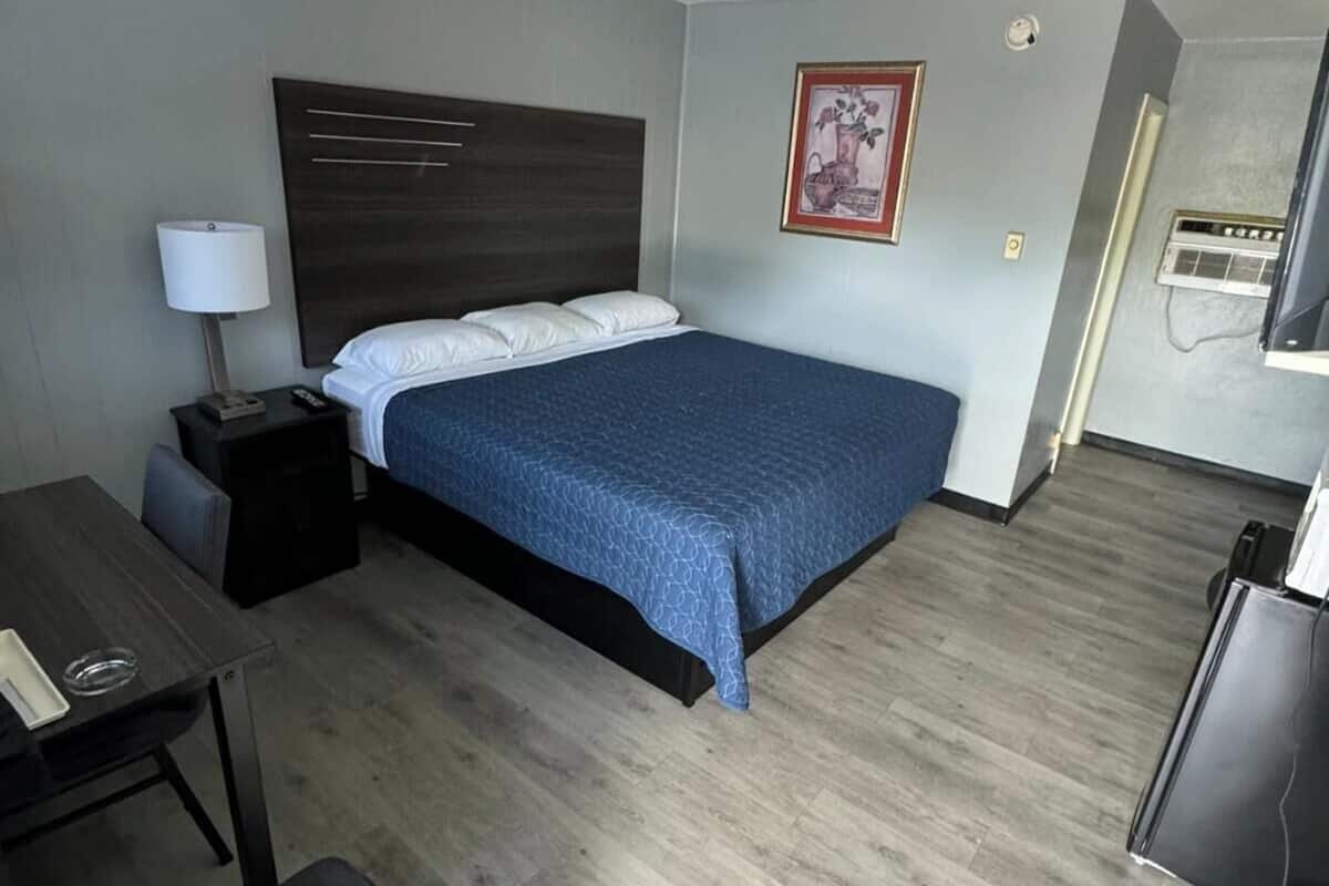 A hotel room with a bed, a desk, a chair, a TV, and a framed picture on the wall.