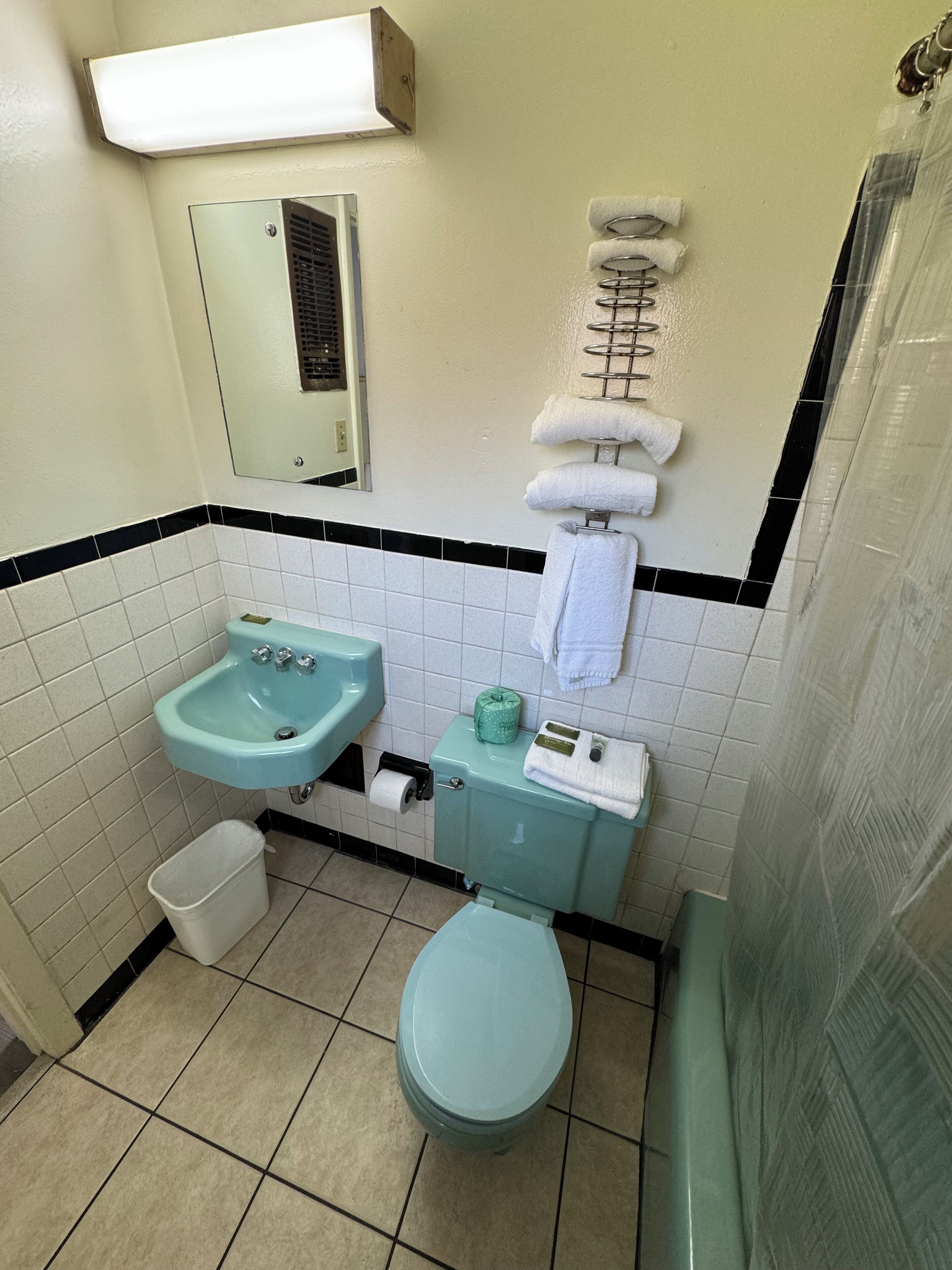 A bathroom with a toilet, sink, and mirror. There is a towel rack with towels and a toilet paper holder.