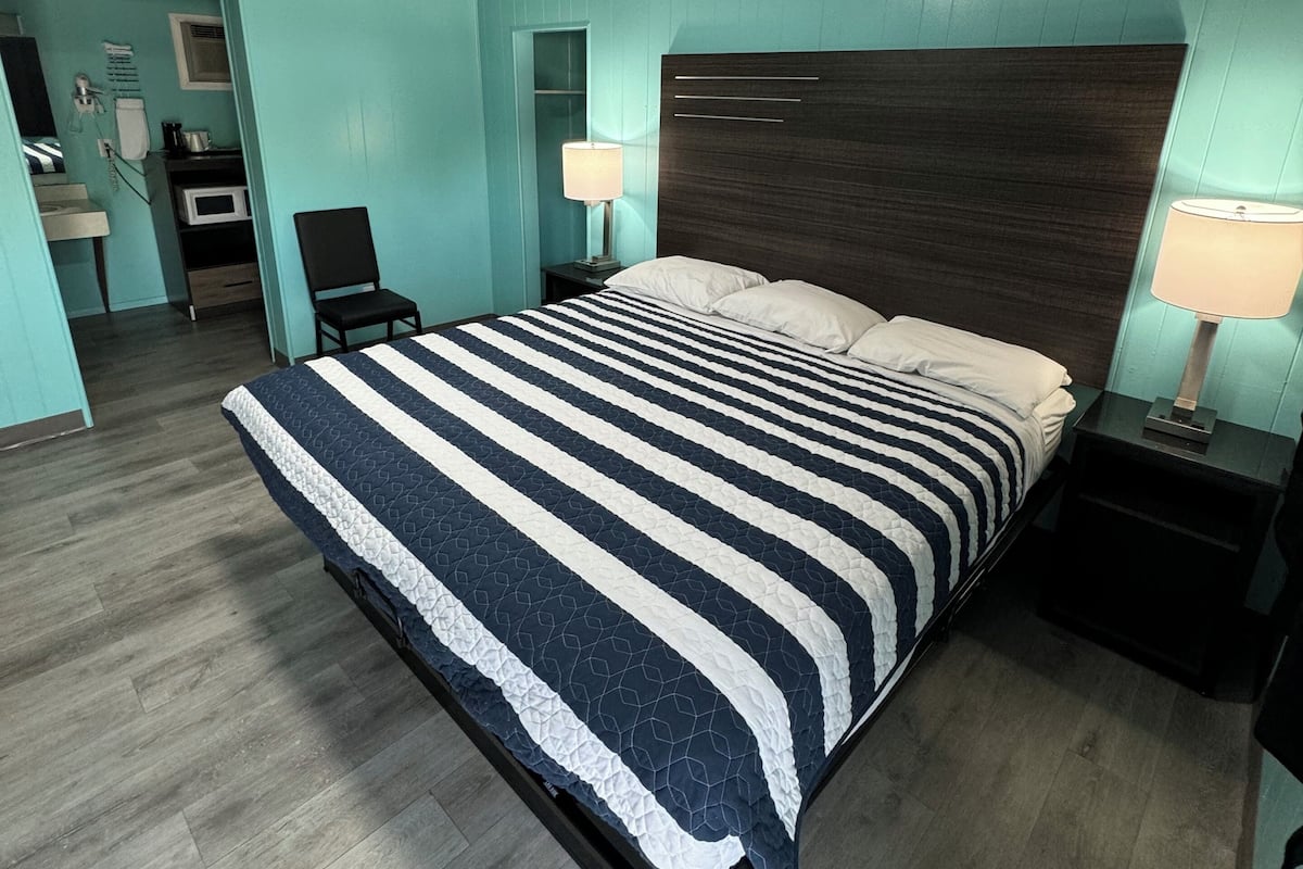 A hotel room with a large bed, a desk, a chair, a microwave, and a small bathroom.