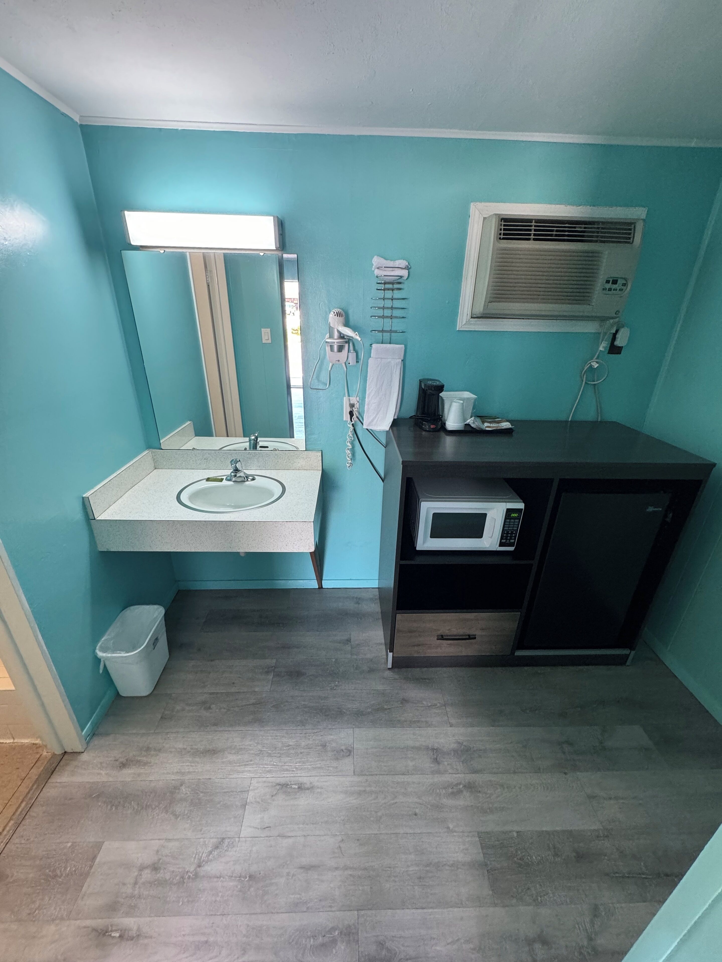A compact bathroom with a sink, mirror, towel rack, hairdryer, and microwave.