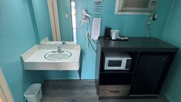 Un baño pequeño con lavamanos, espejo, toallero, secador de pelo y microondas.