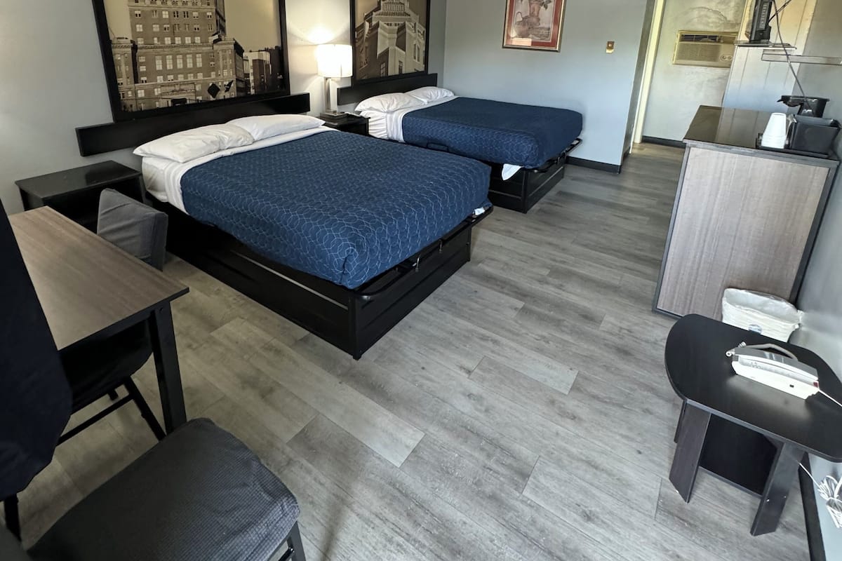 A hotel room with two beds, a desk, a chair, a dresser, and a television.