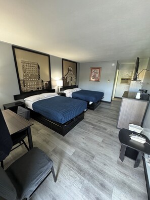 A hotel room with two beds, a desk, a chair, a dresser, and a television. - Acorn Motel (Black Mountain)