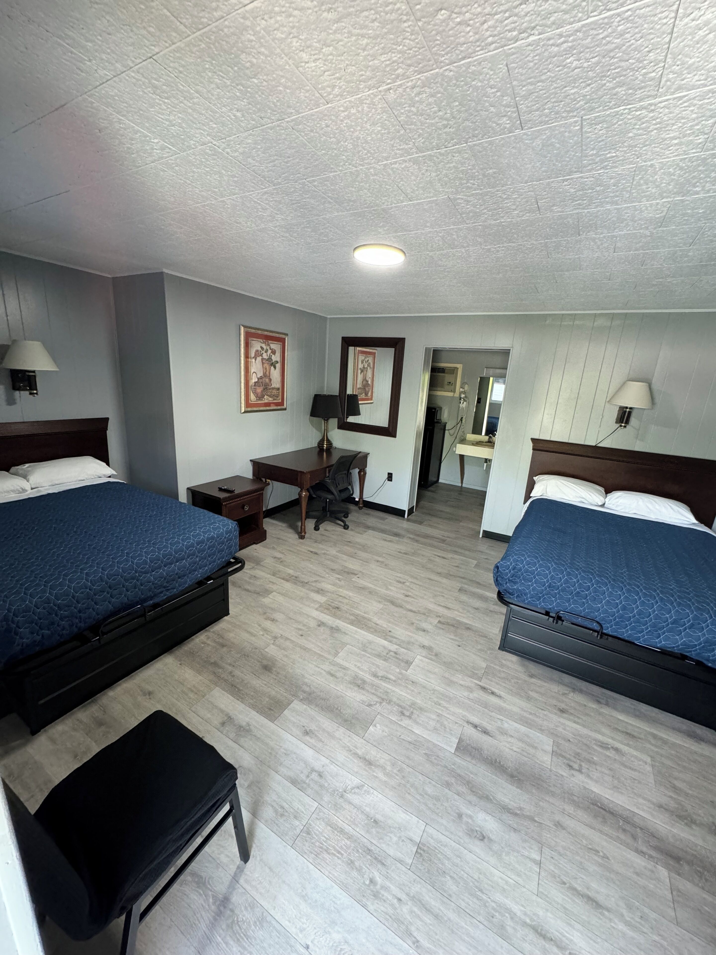 Hotellihuone, jossa on kaksi sänkyä, työpöytä, tuoli ja pieni penkki.
