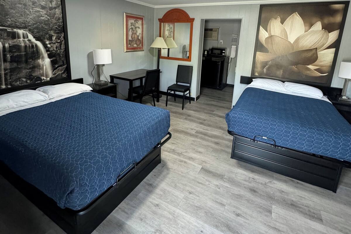 A hotel room with two beds, a desk, a chair, a lamp, and artwork on the walls.