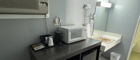 A small bathroom with a sink, mirror, and microwave on a dark countertop.