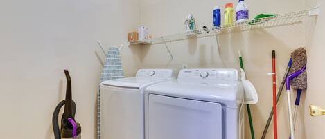 A laundry area with two white washing machines, a vacuum cleaner, and a shelf with cleaning supplies.