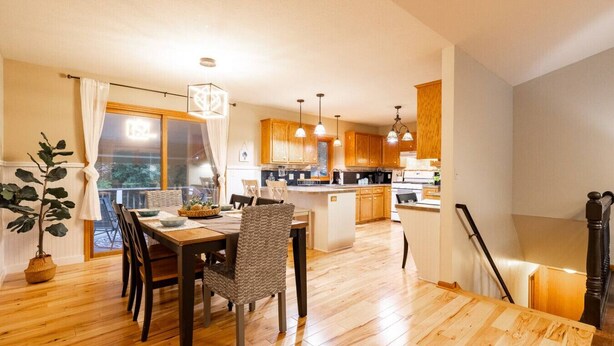 A modern kitchen with wooden cabinets, a dining area with a table and chairs, and a staircase leading to an upper level. - Midlake Elegance Retreat (Hudsonville)