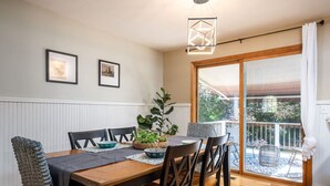 A dining area with a wooden table, chairs, a plant centerpiece, framed pictures on the wall, and a view through a glass door. - Midlake Elegance Retreat (Hudsonville)
