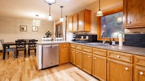 A kitchen with wooden cabinets, a dishwasher, a dining area with a table and chairs, pendant lights, and a window. - Midlake Elegance Retreat (Hudsonville)