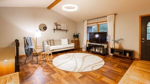 A living room with a sofa, a TV stand, a round rug, and a wooden floor. - Midlake Elegance Retreat (Hudsonville)