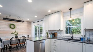 A modern kitchen with white cabinets, a stainless steel dishwasher, and a dining area with a wooden table and chairs.