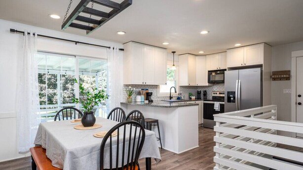 A modern kitchen with white cabinets, a central island, and a dining area with a table and chairs.