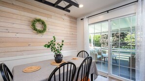 A dining area with a wooden wall, a black pot with green plants, and a large sliding glass door leading to an outdoor patio.