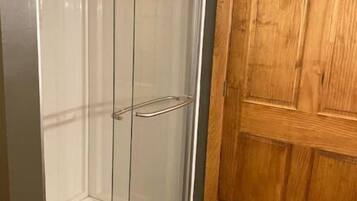 Un vestidor con puerta de madera y cabina de ducha de vidrio.