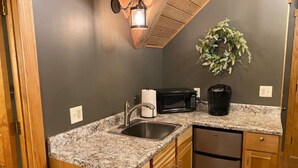 Cocina compacta con encimeras de granito, armarios de madera, pileta de acero inoxidable, microondas y cafetera.