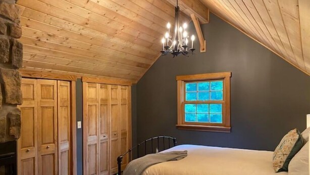 Un dormitorio con una cama grande, techo de madera, pared de piedra y una ventana con vidrios azules.