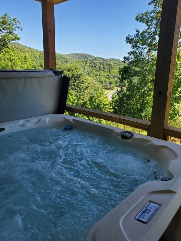 Un bain à remous avec une terrasse en bois et une vue sur une colline boisée.