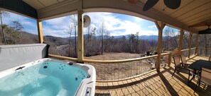Un bain à remous sur une terrasse en bois, avec vue sur une forêt et des montagnes.