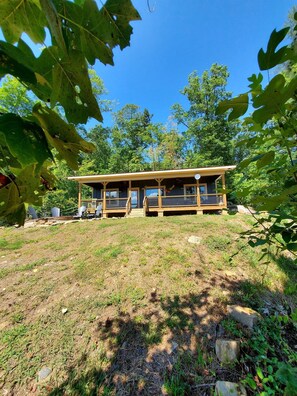 Une cabane dotée d’une véranda, entourée d’arbres et bordée d’une pelouse.