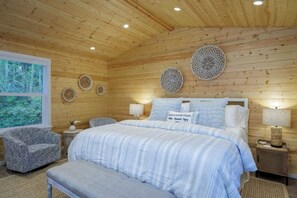 Un dormitorio de cabaña de madera con una cama, dos mesitas de noche, una silla y placas decorativas en la pared.