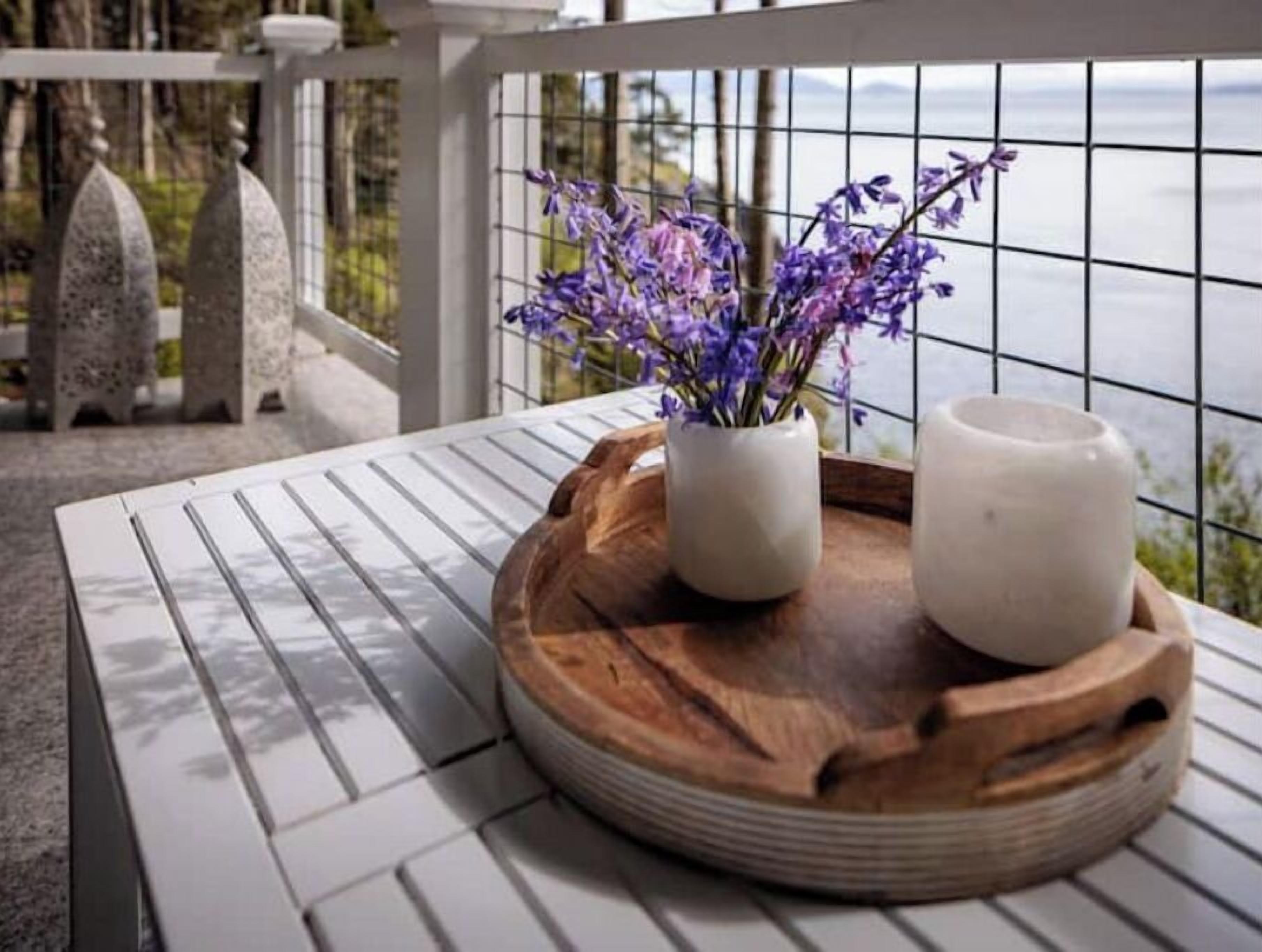 Uma mesa branca com uma bandeja de madeira que contém dois vasos brancos com flores roxas.