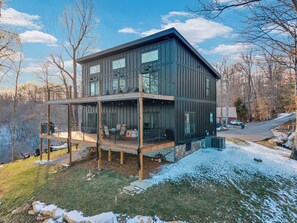 Une maison moderne à deux étages, dotée d’une terrasse et de grandes fenêtres, entourée d’arbres et offrant une vue sur un paysage enneigé.