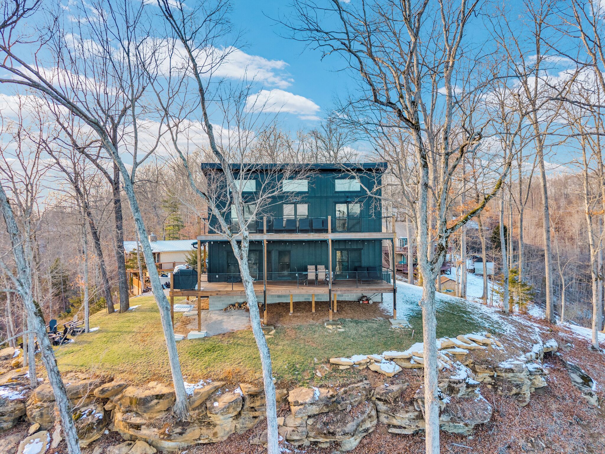 Une maison moderne à deux étages, dotée d’une terrasse et entourée d’arbres, avec un paysage rocheux en toile de fond.