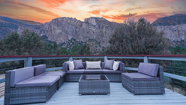 En terrasse med en hjørnesofa og sofabord, med udsigt til et bjergrigt landskab.