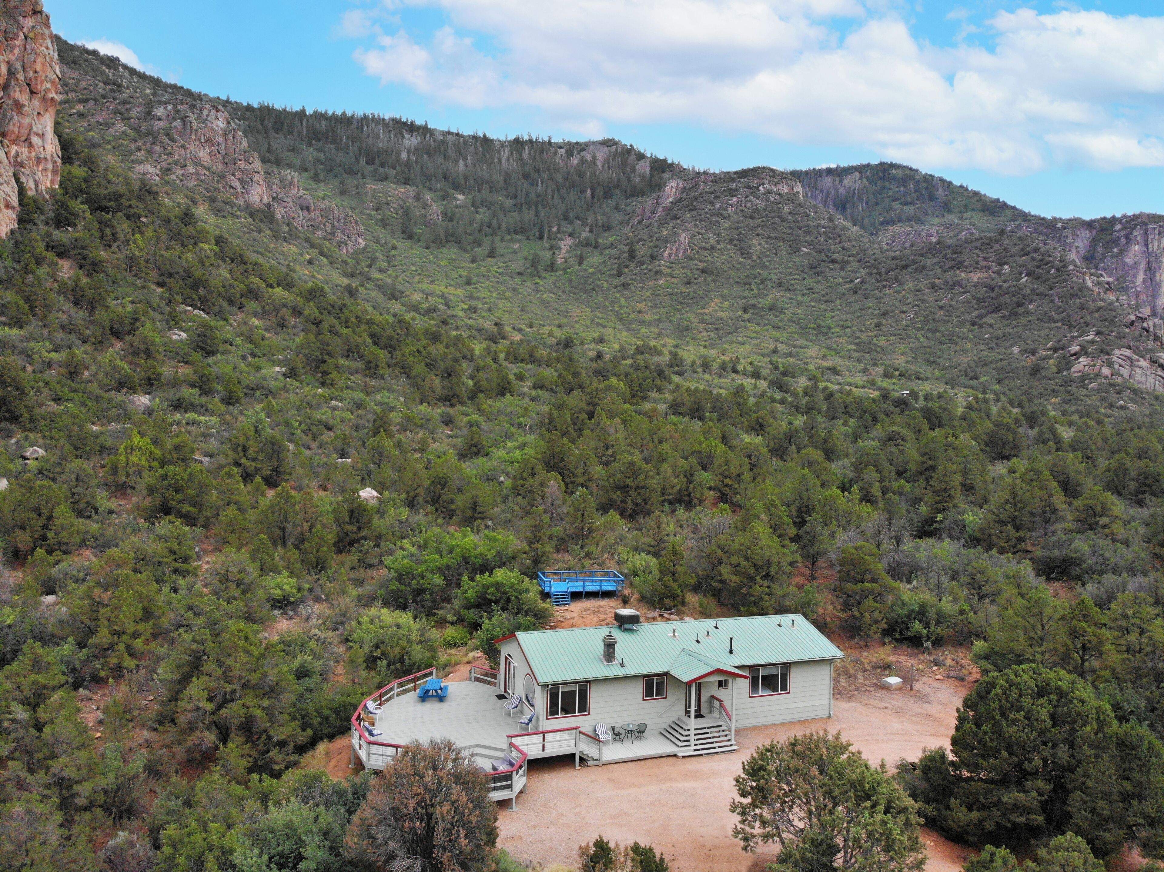 A house with a green roof, a deck with outdoor seating, and a dirt driveway.