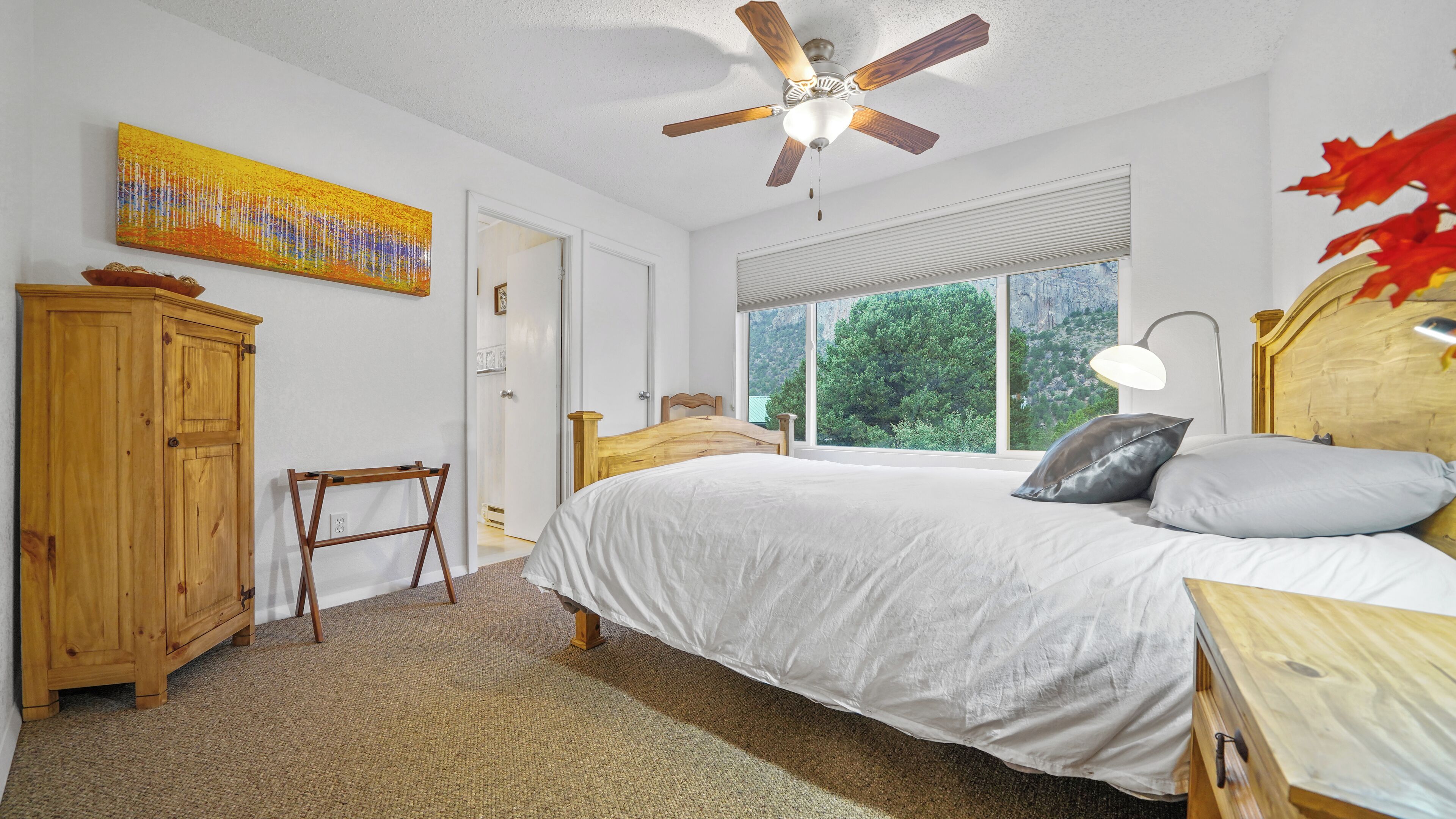 Quarto com cama, ventoinha no teto, janela com vista, armário de madeira e um quadro.