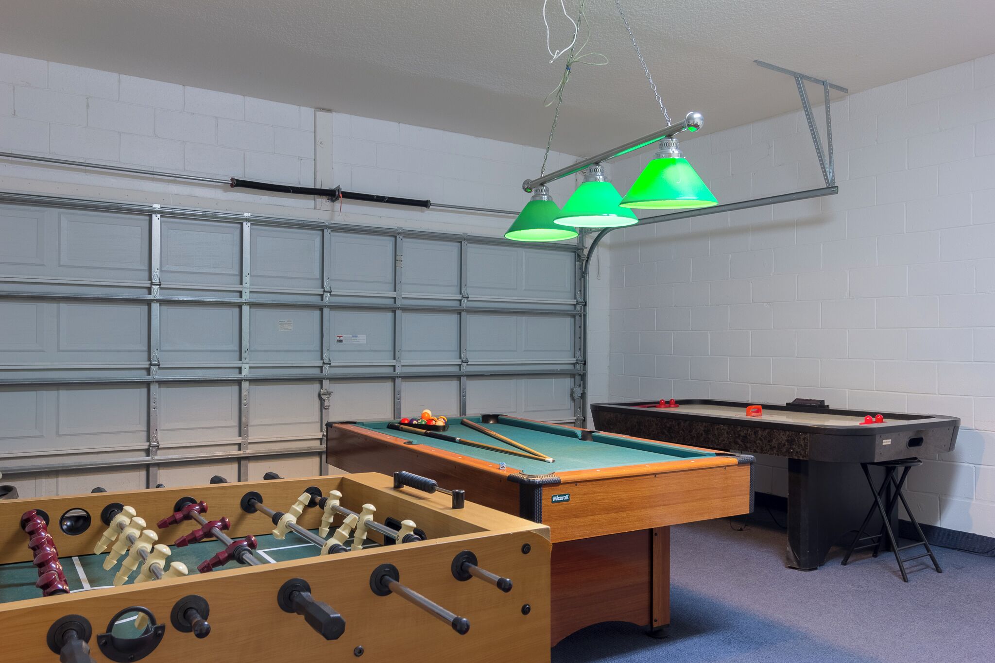 A room with a foosball table, pool table, and a bar area.