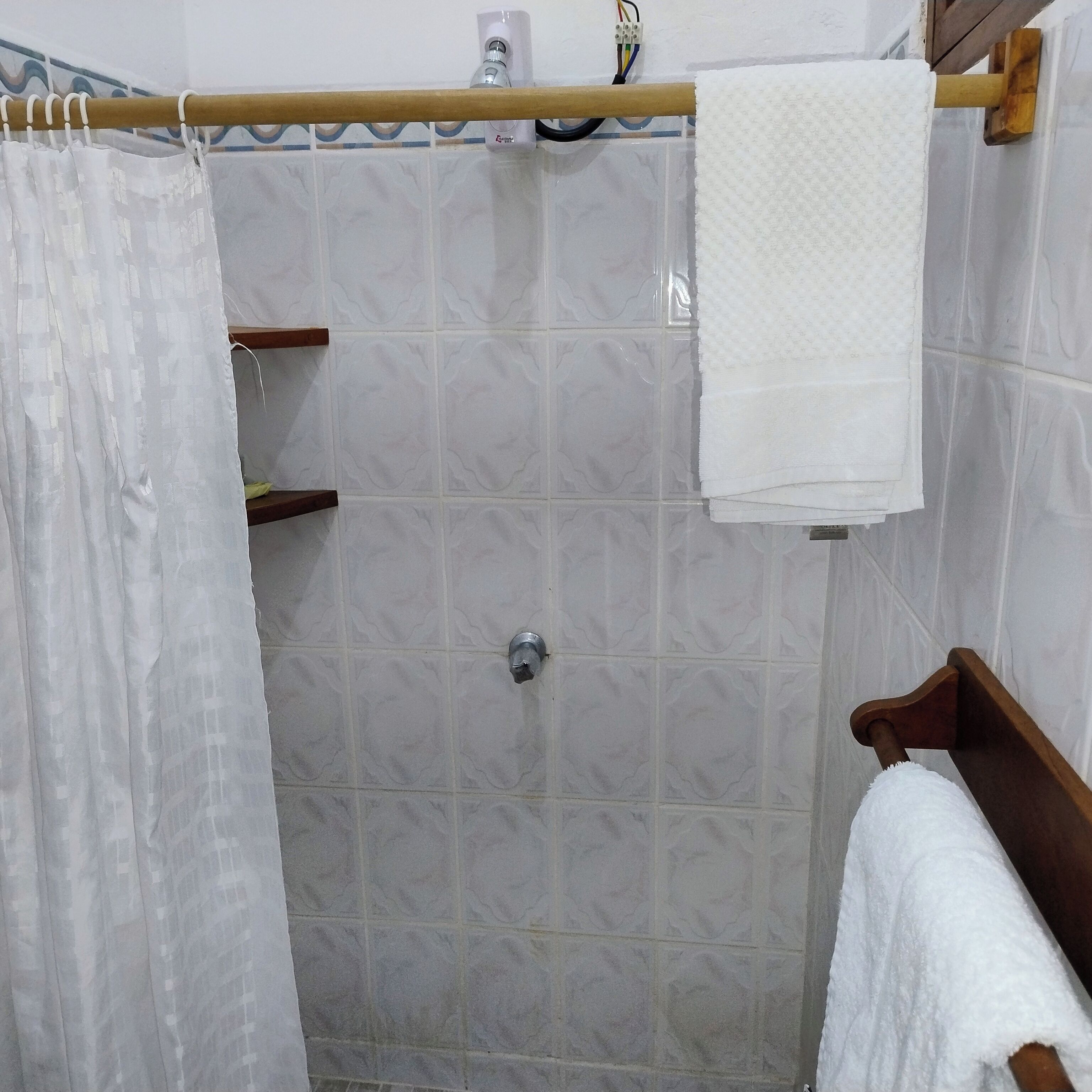 A shower area with a tiled wall, a showerhead, a towel rack, and a shower curtain.