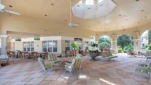 A spacious indoor area with tiled flooring, multiple seating arrangements, ceiling fans, and a variety of shops in the background. - Villa Holidays 7704 WH (Kissimmee)